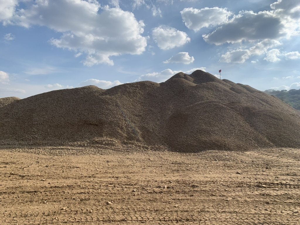 A large stockpile of crushed material under a blue sky