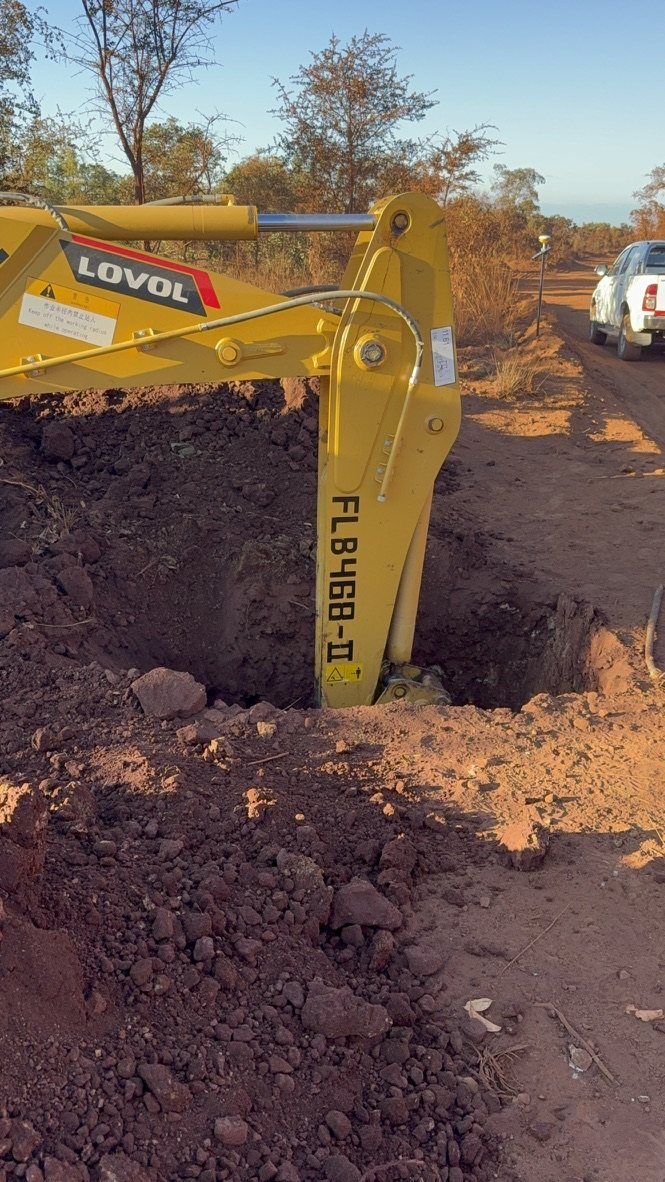 An excavator digging a sampling pit beside the access road