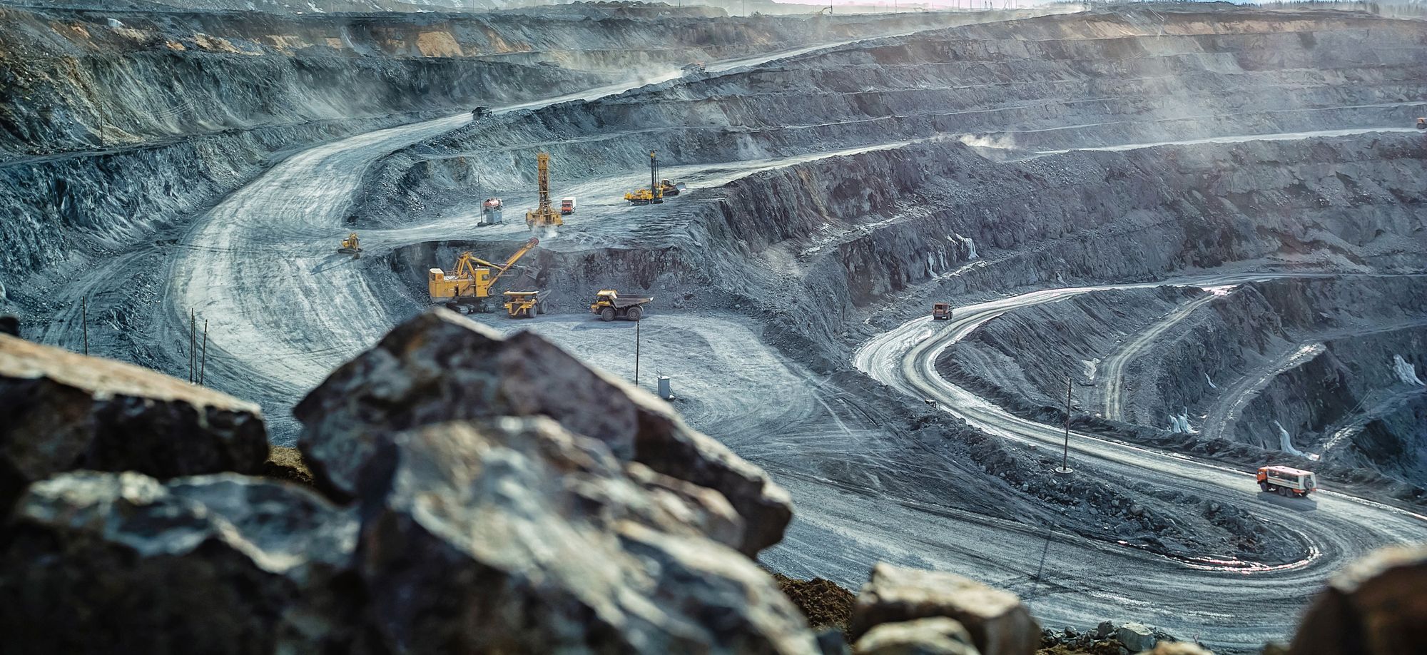 Wide view of a terraced open pit with haul roads, drills and trucks at work