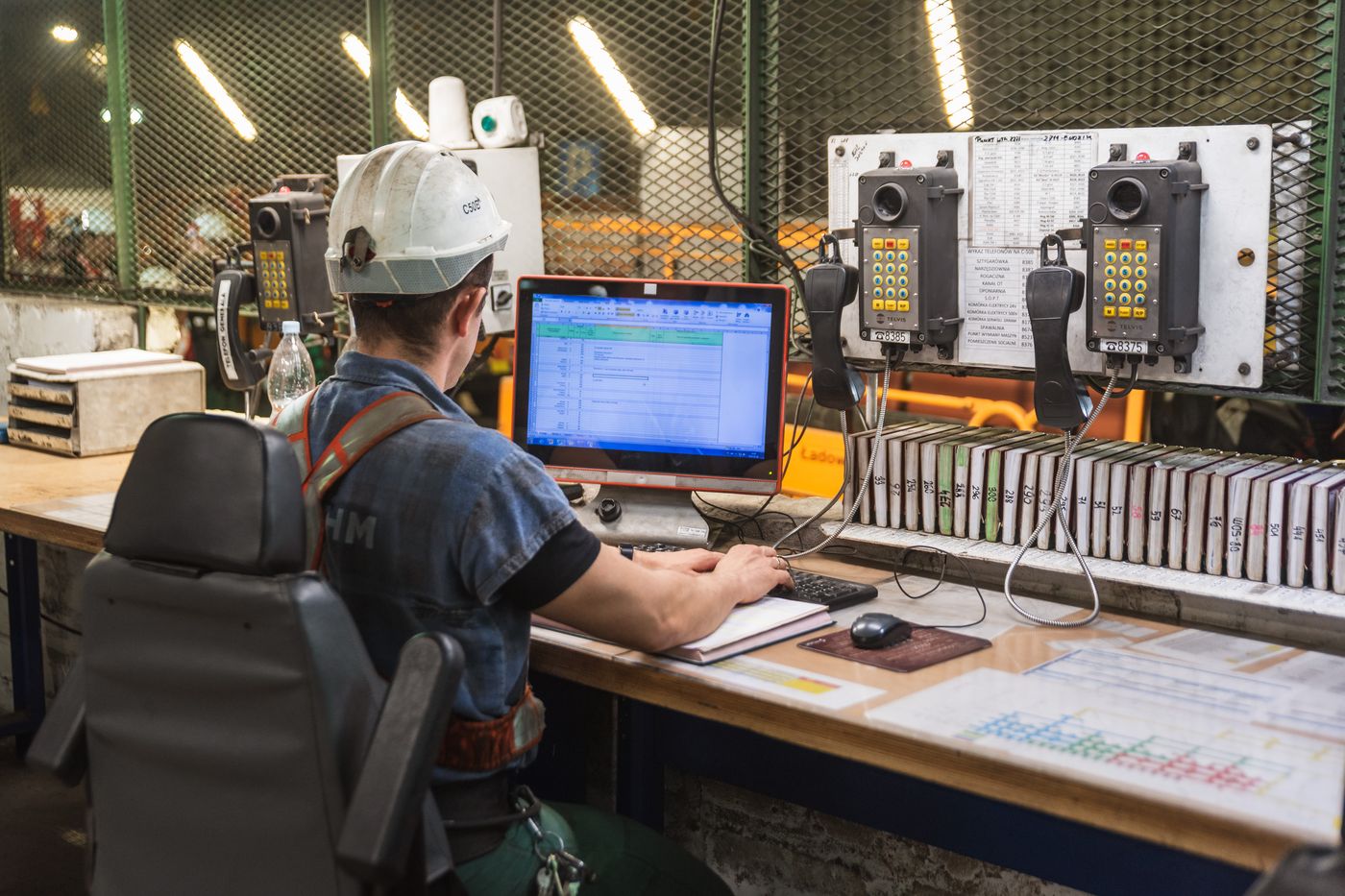 A site controller in a hard hat checking records at a mine control desk